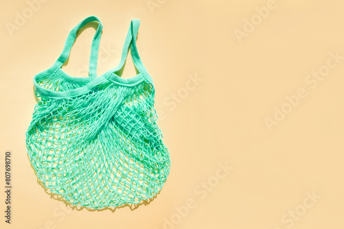 Reusable blue-green mesh bag on a beige background in sunny daylight. Mesh shopping bags. Sustainable use concept