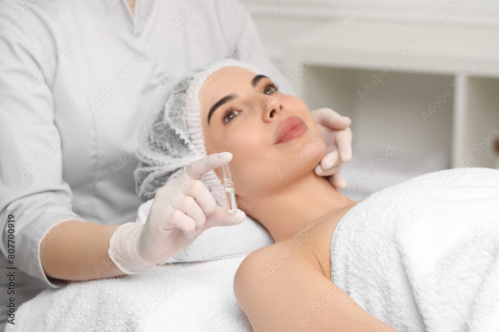Professional cosmetologist holding skincare ampoule while working with client in clinic, closeup Professional cosmetologist holding skincare ampoule while working with client in clinic, closeup