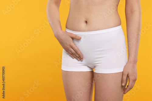 Woman holding hand near panties on orange background, space for text. Women's health © New Africa