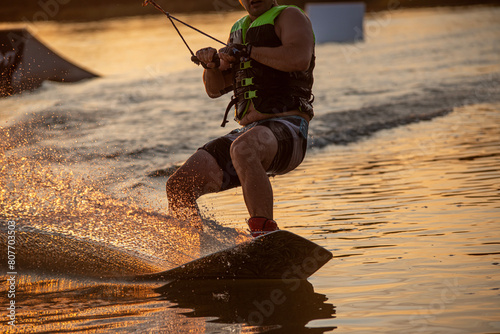Wakeboarder making tricks. Low angle shot of man wakeboarding on a lake. Man water skiing at sunset. photo