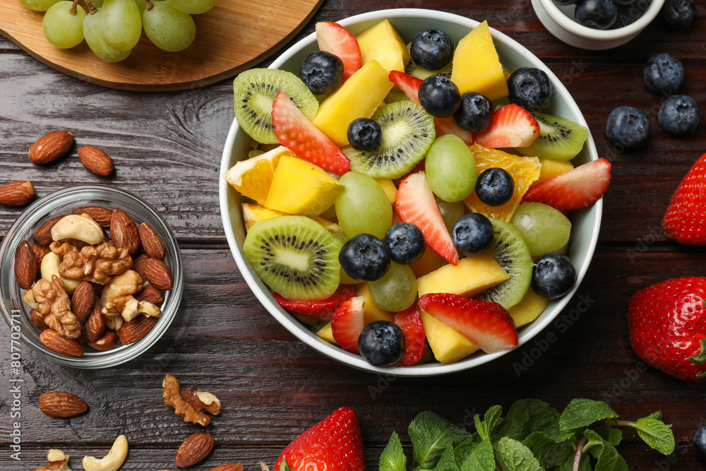 Tasty fruit salad in bowl and ingredients on wooden table, flat lay Tasty fruit salad in bowl and ingredients on wooden table, flat lay