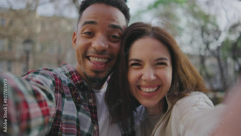 POV shot of caucasian woman and african american man couple making a selfie video on smartphone. They smiling, laughing together on street. Guy and girl are in love with each other