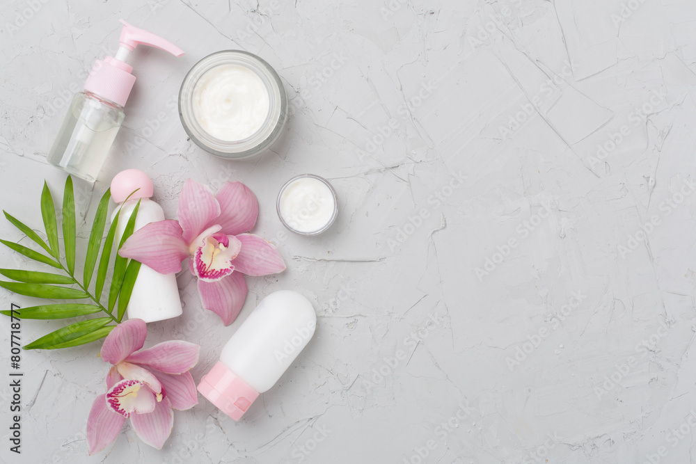 Bottles and jars with cream and orchids on concrete background, top view Bottles and jars with cream and orchids on concrete background, top view