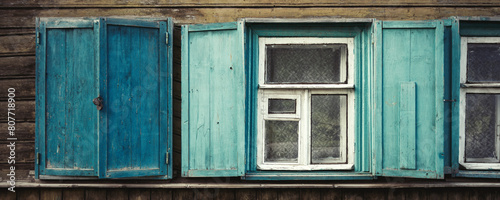 Windows in an old wooden house. Open and closed shutters on the windows. Weathered, faded paint on the wall of the house and on the shutters. Country style. Wide panorama for design and background. photo