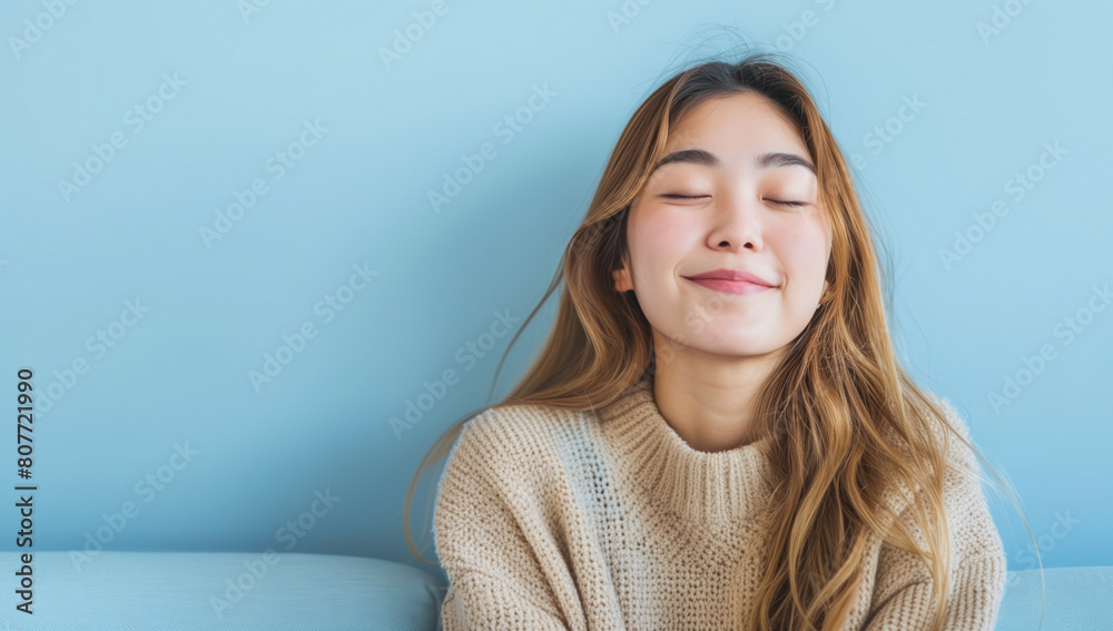 A smiling beautiful asian woman with long hair sitting on sofa and with closed eyes, dreamy facial expression. A smiling beautiful asian woman with long hair sitting on sofa and with closed eyes, dreamy facial expression.