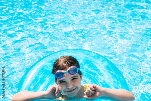 A little girl with an inflatable circle jumped into the pool. A cute kid in a swimsuit