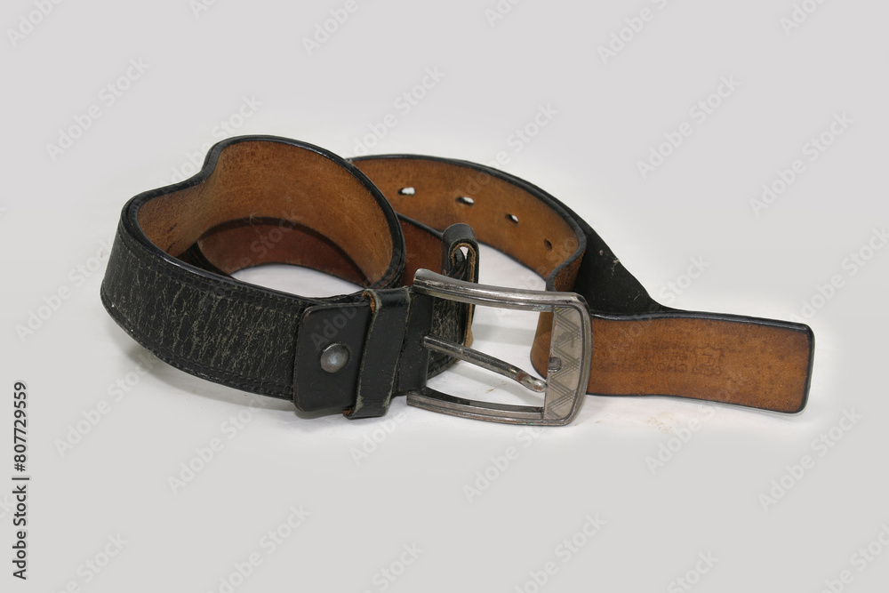 Obraz premium Used and Old black leather belt with buckle isolated on white background.