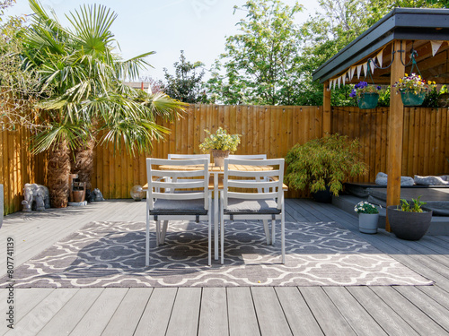 Minimalistic English modern garden with table and chairs. Sunny summers day with green plants and decking on the patio