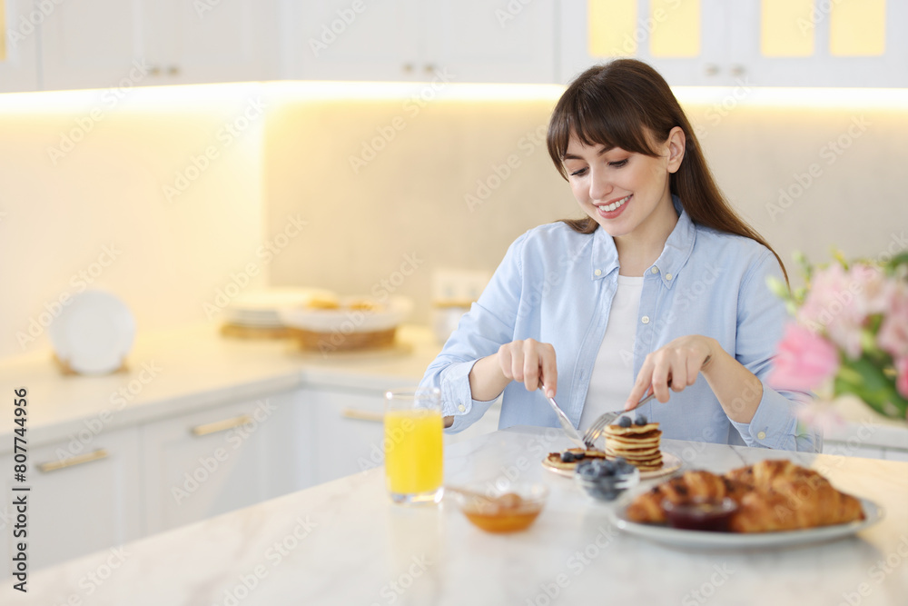 Smiling woman eating tasty pancakes at breakfast indoors. Space for text