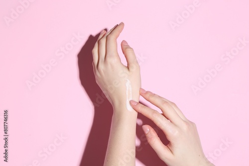 Woman applying cream on her hand against pink background  closeup