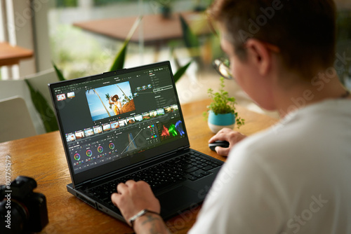 Professional video colorist adjusts footage colors on laptop in bright office. Creative industry editor works on film grading, enhances visual appeal. Expert uses software for post-production.