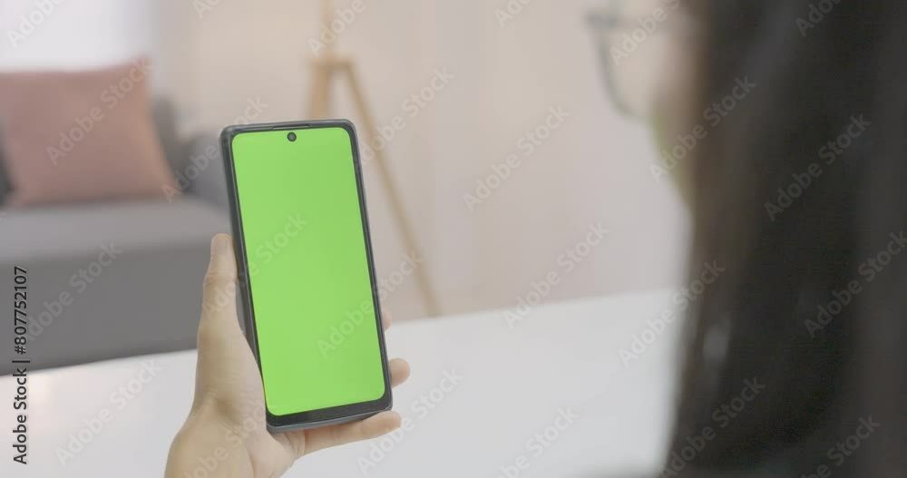 Use green screen for copy space closeup. Chroma key mock-up on smartphone in hand. Woman holds mobile phone and swipes photos or pictures left indoors of cozy home.