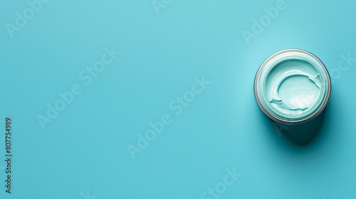 A blank cosmetic cream jar on the right side of a solid blue background with copyspace on the left