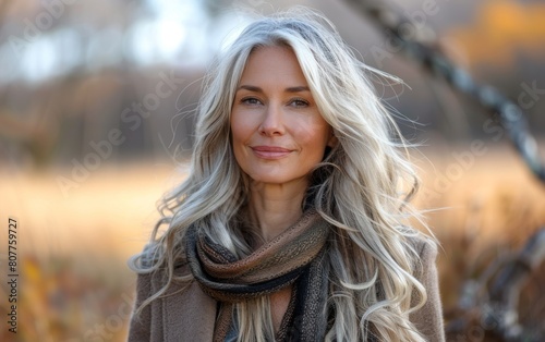 A woman with long hair and a scarf is smiling. She is wearing a brown coat and scarf