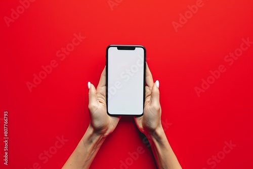 A person is holding a white phone in their hand on a red background. Concept of simplicity and minimalism, as the phone is the only object in focus. Mockup photo
