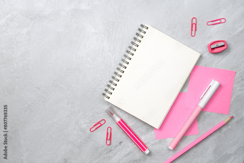 Notebook and pink sticky note and stationery on stone texture background. Work desk space