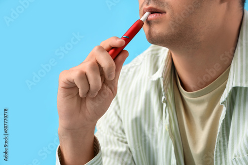 Young man smoking electronic cigarette on blue background, closeup