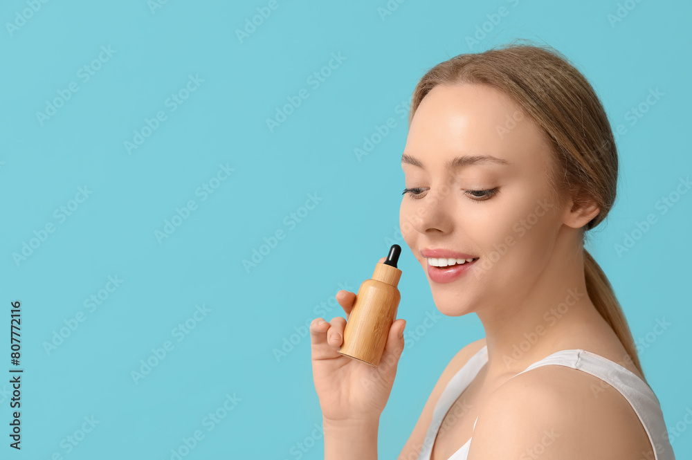 Beautiful young woman with bottle of cosmetic oil on blue background Beautiful young woman with bottle of cosmetic oil on blue background