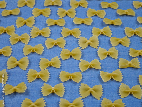 IItalian uncooked white farfalle pasta are laid out in rows on light blue fabric, natural decorative background photo