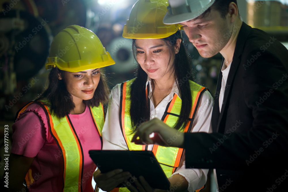 Three worker wearing safety vest and helmet are looking at a tablet computer in an industrial environment. Three worker wearing safety vest and helmet are looking at a tablet computer in an industrial environment.