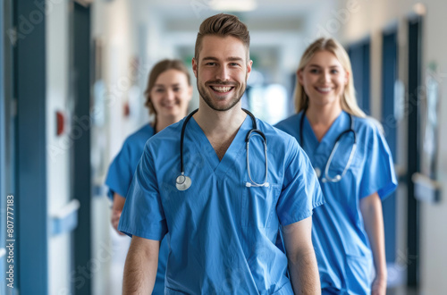 A group of happy male and female nurse in blue scrubs walking down the hospital hallway smiling at camera