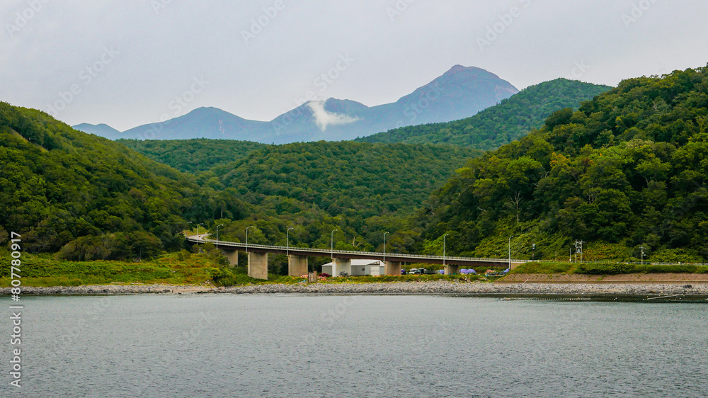 A picturesque view from the sightseeing cruiser overlooking the Horobetsu Bridge at the mouth of the Horobetsu River and Mount Tenchozan in the Shiretoko Peninsula, Hokkaido, Japan.