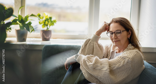 Caucasian attractive mature middle aged woman with glasses relaxing while sitting on sofa at home © olezzo