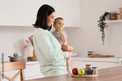Mother giving her little baby nibbler with food in kitchen photo