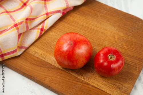Cutting board with several pink tomatoes and red kitchen towel on white wooden background..