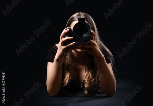Obraz na plátne Female photographer with modern camera taking picture of viewer on black backgro
