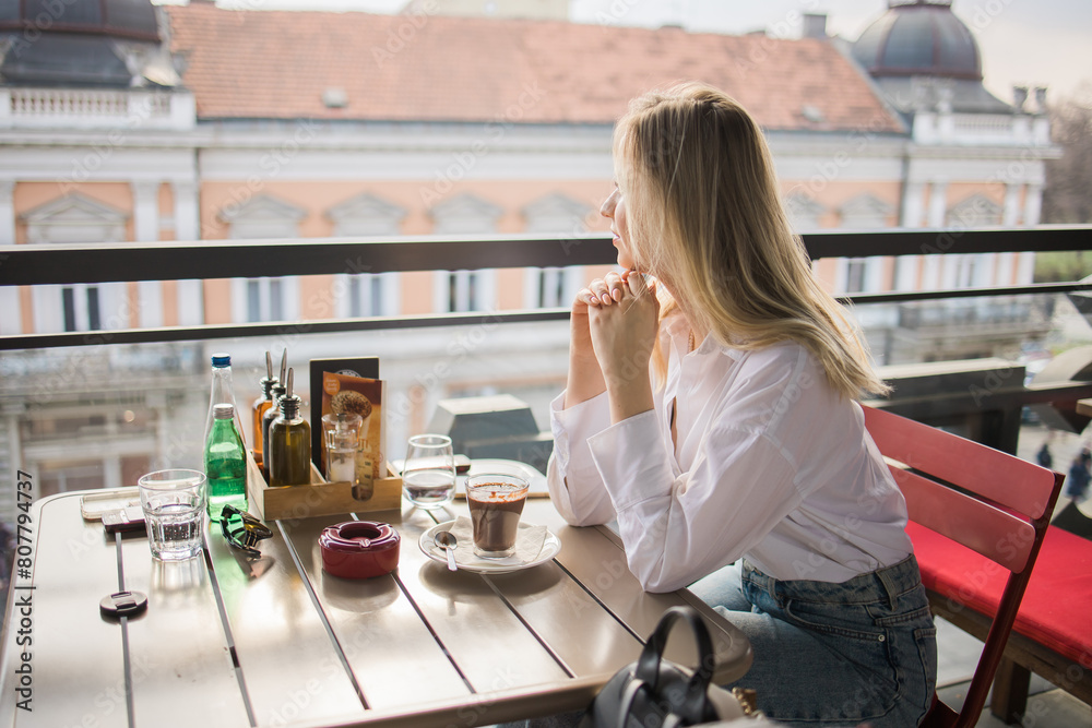 Gen z blonde woman drinks hot chocolate in summer cafe. Tasty beverage and break concept. Generation z people