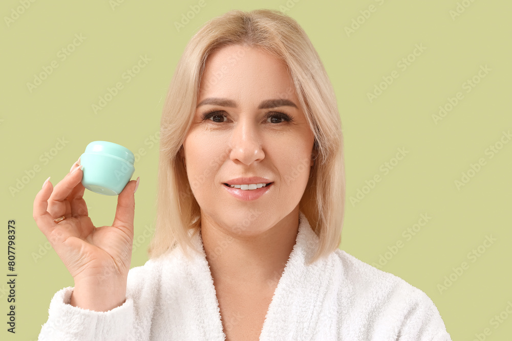 Beautiful mature woman in bathrobe with jar of cream on green background Beautiful mature woman in bathrobe with jar of cream on green background
