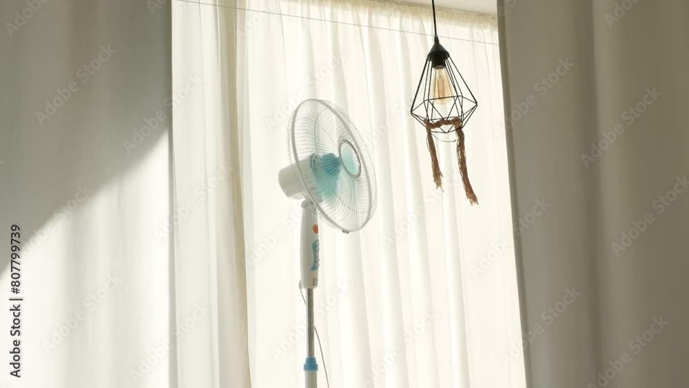 Fan on a background of white curtains. The summer propeller develops the curtains from the air flow. It's hot outside in the summer. Cooling the room with air conditioning. Fan on a background of white curtains. The summer propeller develops the curtains from the air flow. It's hot outside in the summer. Cooling the room with air conditioning.