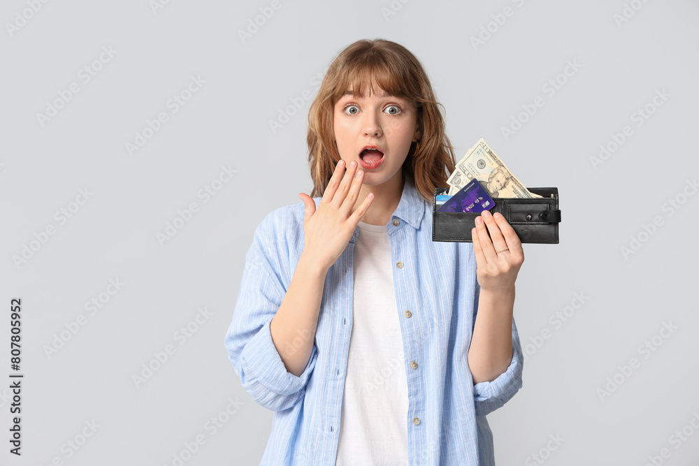 Surprised young woman holding wallet with money and card on grey background Surprised young woman holding wallet with money and card on grey background