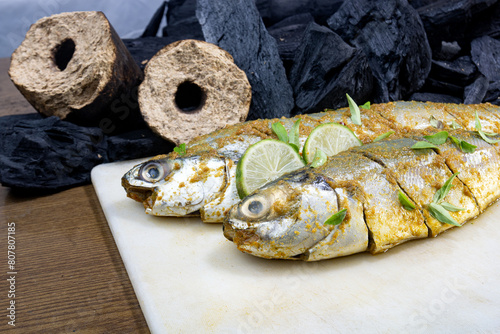 Fish BBQ. Marinated fish with salt pepper, green chili and turmeric powder. wooden coal and Charcoals in background. photo