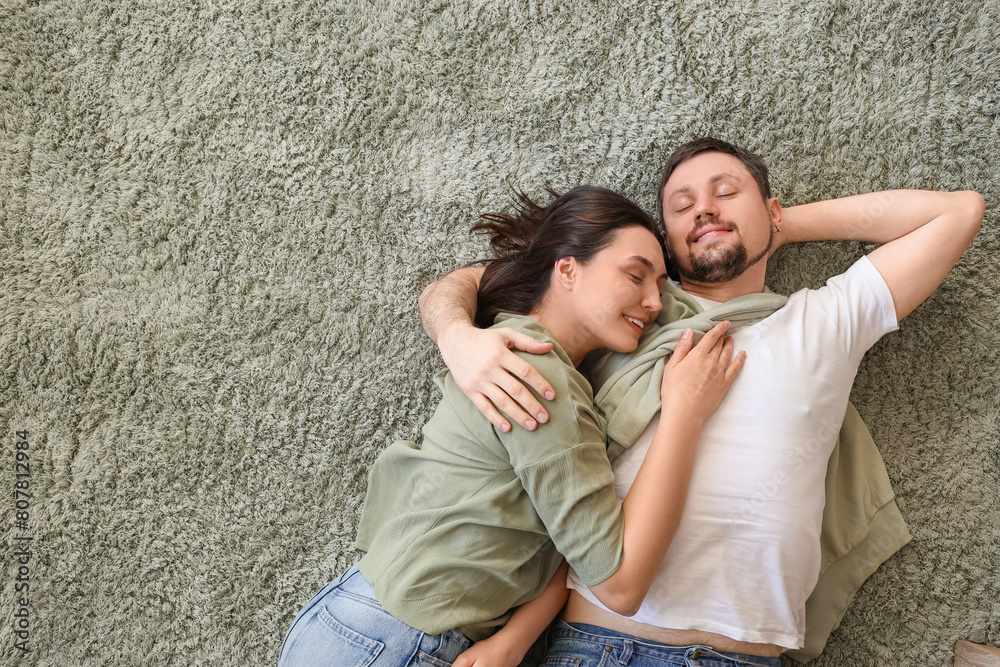 Young couple hugging on green carpet at home, top view