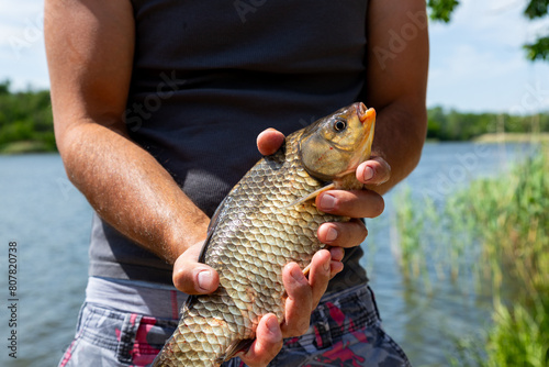 Fisherman holding Prussian Carp fish in hands on the lake photo
