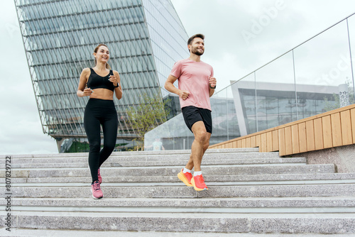 An energetic couple runs up the stairs in an urban environment  their workout intensified by the modern architectural background and their lively expressions.