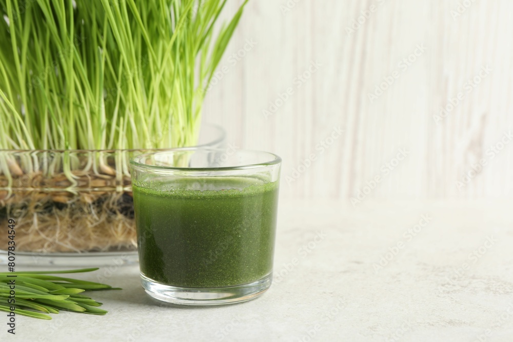 Wheat grass drink in glass and fresh sprouts on light table, space for text Wheat grass drink in glass and fresh sprouts on light table, space for text