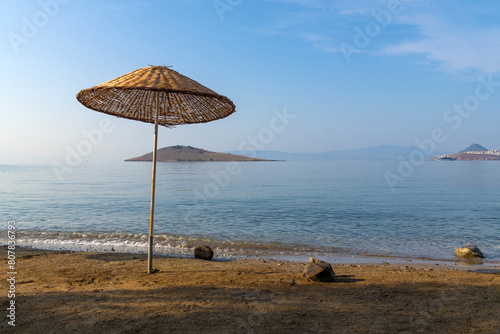 Close-up of a braided beach umbrella on the shore of a sandy beach against the background of a small island in the sea early in the morning. Beautiful marine tourist landscape