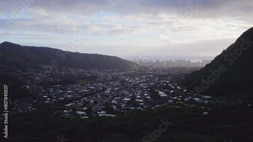 establishing shot of a small residential island town nestled between two rainforest covered mountains with the city view on the horizon in the ravine on the island of Oahu Hawaii in late afternoon photo