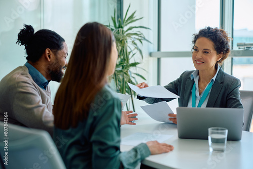 Happy insurance agent going through paperwork with her clients in office.