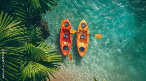 A top-down view of two bright orange kayaks floating in the clear turquoise waters of a tropical sea, surrounded by lush green palm fronds. Summer concept, copy space. photo