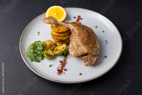 Duck leg confit with Brussels sprouts, baked potatoes, thyme and orange. Traditional French cuisine. Selective focus, close-up, black background.