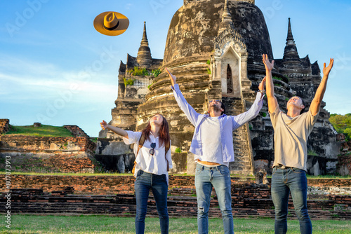 cheerful tourists doing hands up,a woman throw a hat up to sky,all of them laughing and feeling freedom,young diverse friends visiting at Wat Phra Si Sanphet, Ayutthaya historical park,Thailand