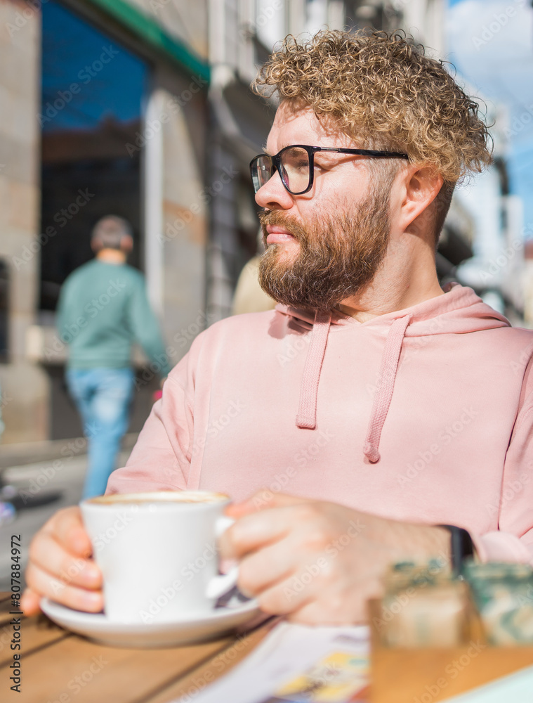 Young bearded man having breakfast at table of street cafe on spring day, drinking warm cappuccino and enjoy morning. Young bearded man having breakfast at table of street cafe on spring day, drinking warm cappuccino and enjoy morning.