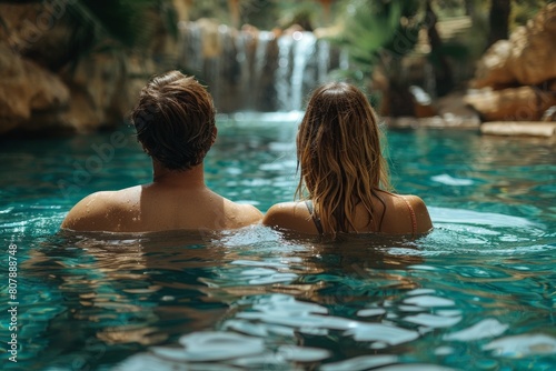 A man and woman are swimming in a pool with a cascading waterfall in the background