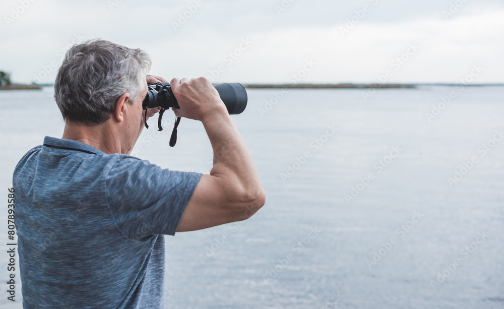 Obraz premium European Mature man looking in a binoculars . Hobby and recreation concept