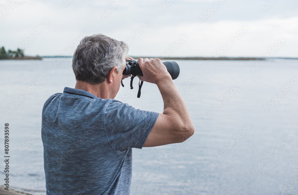 Obraz premium European Mature man looking in a binoculars . Hobby and recreation concept