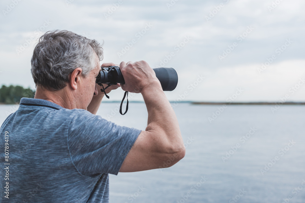 Obraz premium European Mature man looking in a binoculars . Hobby and recreation concept